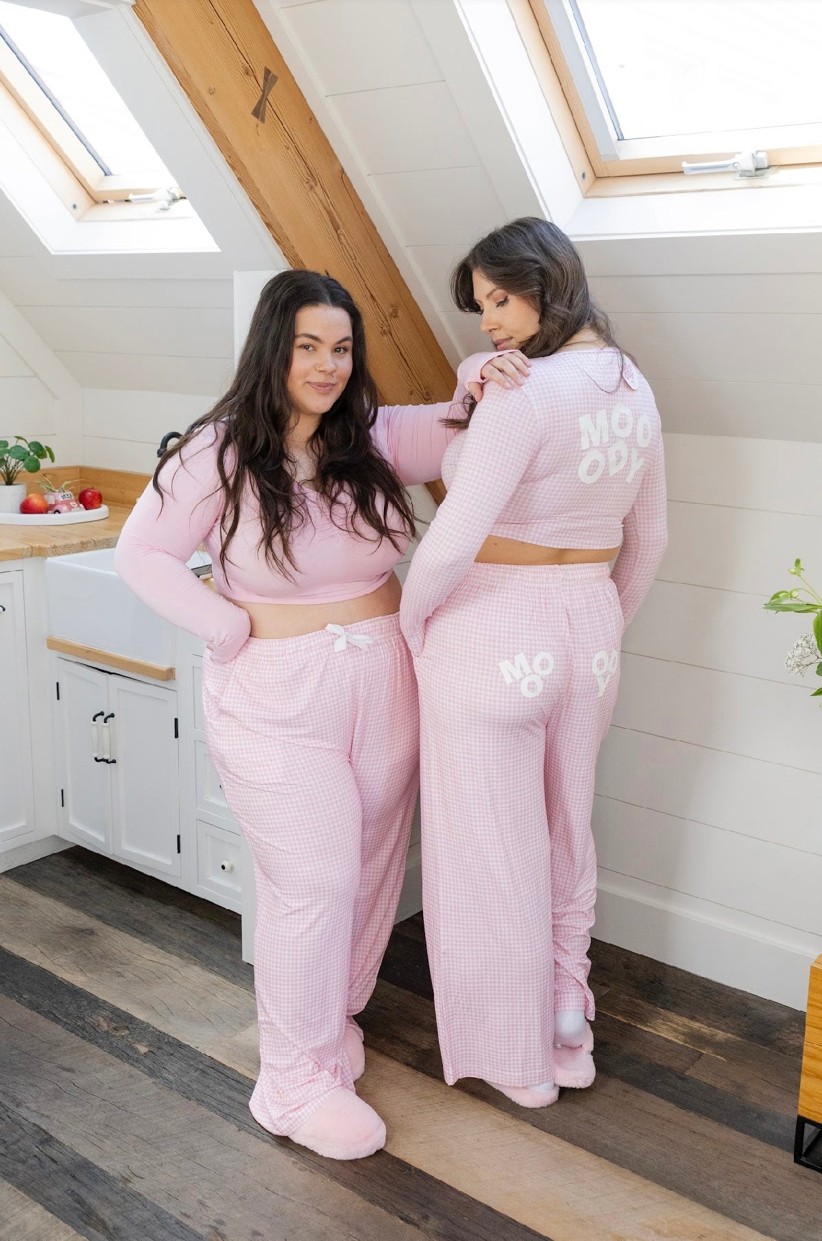 Two women wearing Mooody's bamboo long pyjama pants in pink and white houndstooth. Wearing matching fitted long sleeve cropped top posing.